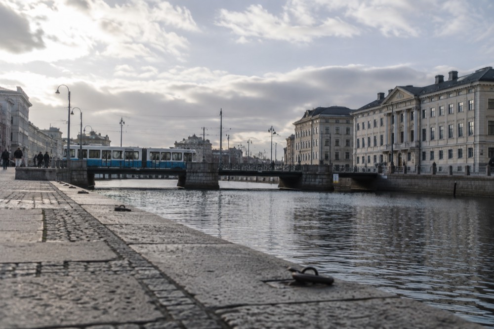 Trams and stone buildings along a Gothenburg canal under a grey Nordic sky