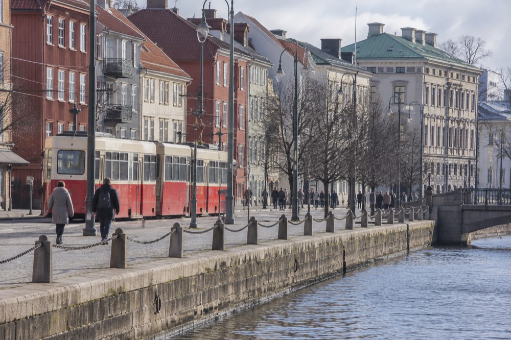 Red tram passing painted wooden houses on a cobblestone street in Gothenburg