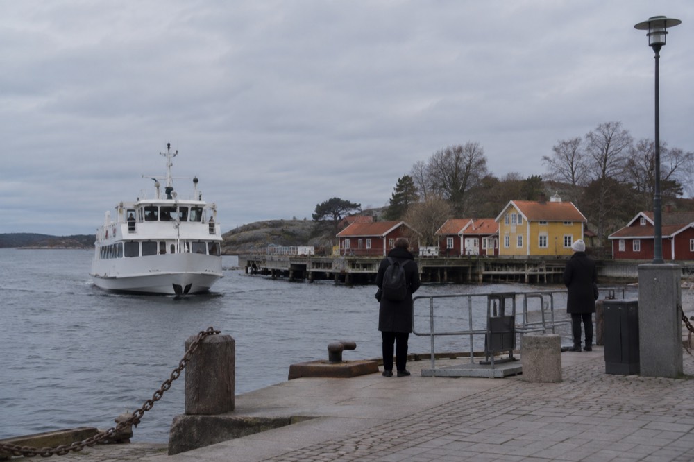 A white Gothenburg archipelago ferry approaching a small car-free island dock with wooden cottages