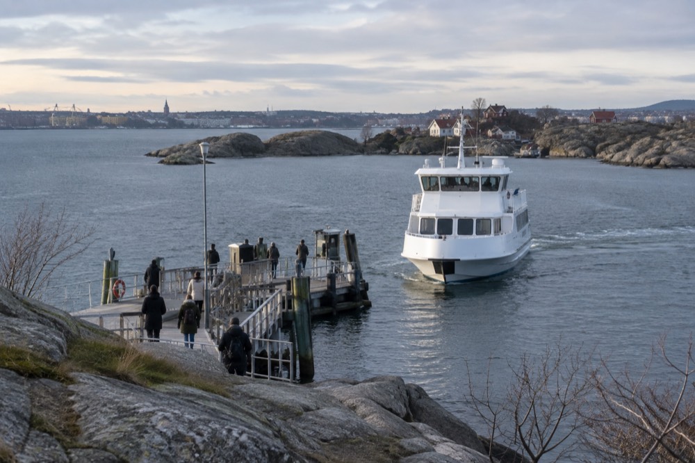 A white passenger ferry approaching a wooden jetty at a rocky island in the Gothenburg archipelago