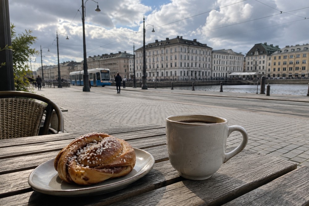 A cinnamon bun and a cup of coffee on a wooden cafe table in soft Nordic light