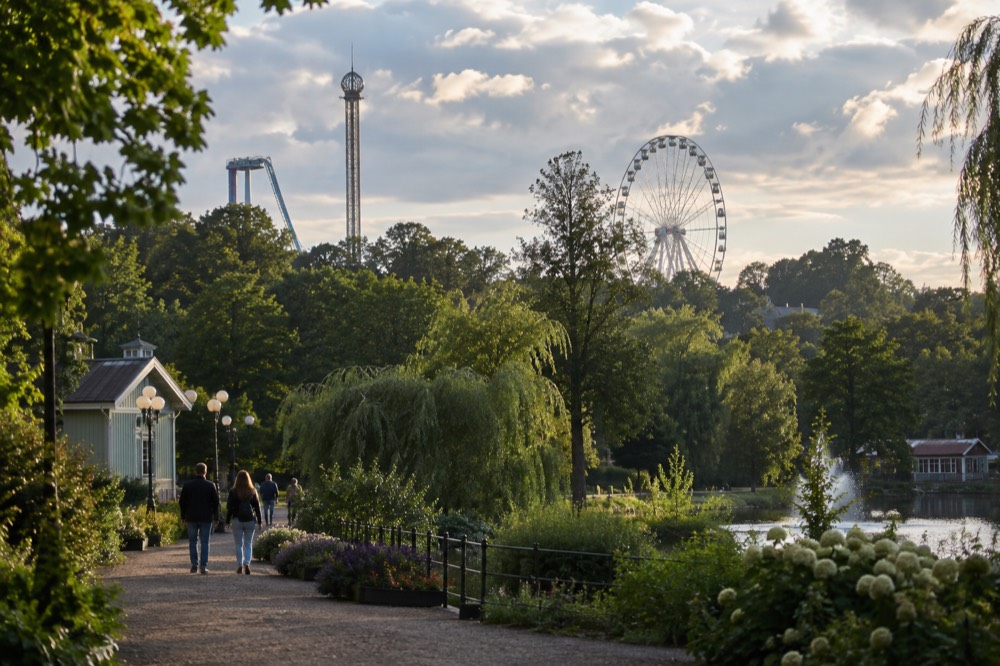 Ferris wheel and amusement park rides rising above tree tops under a bright evening sky in central Gothenburg