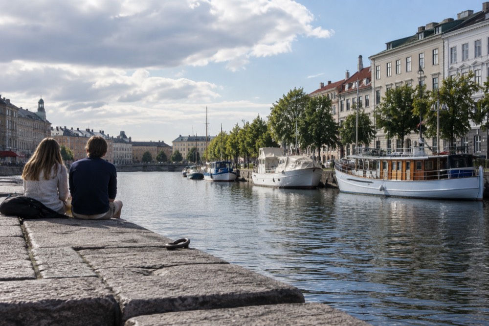 A Gothenburg canal with moored boats and painted wooden houses under a bright summer sky