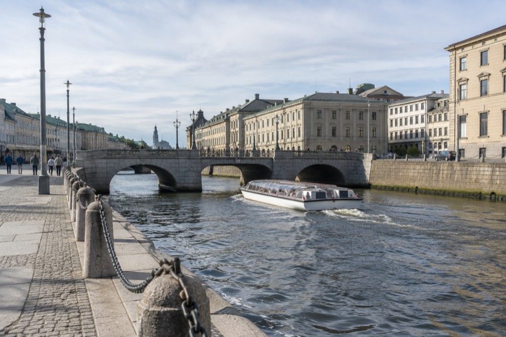 A canal sightseeing boat passing under a stone bridge in central Gothenburg, old stone buildings on both banks