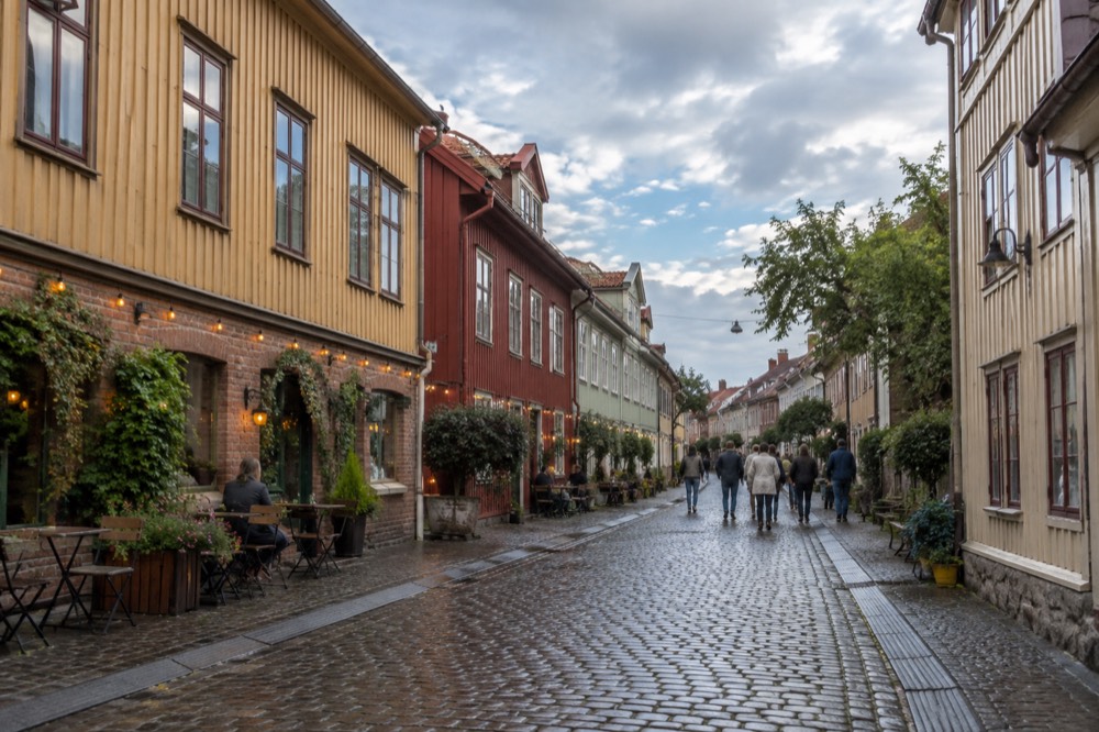 Cobbled pedestrian street in Haga lined with low wooden and brick houses, cafés with outdoor tables and people strolling