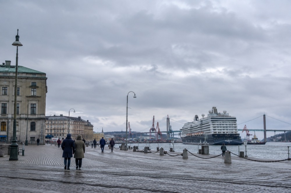 A large cruise ship moored at a quay in Gothenburg harbour with cranes and the Älvsborg bridge in the background