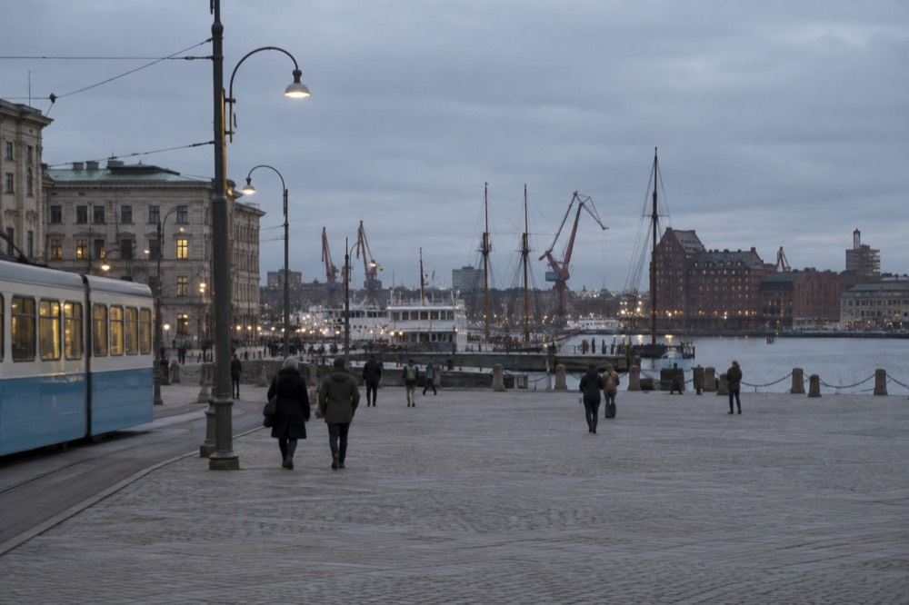 Low evening light over Gothenburg's harbour with cranes, masts and red brick warehouses along the water