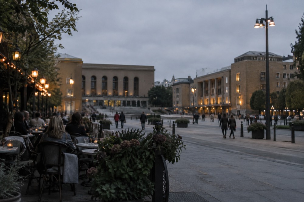 Outdoor restaurant tables along Avenyn in the evening with people seated and streetlights on