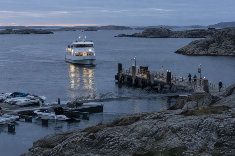 A Västtrafik passenger ferry approaching a wooden jetty between rocky islands