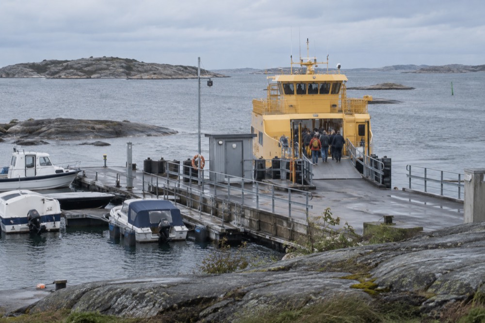 Passengers boarding a yellow ferry at a small island jetty on a grey morning
