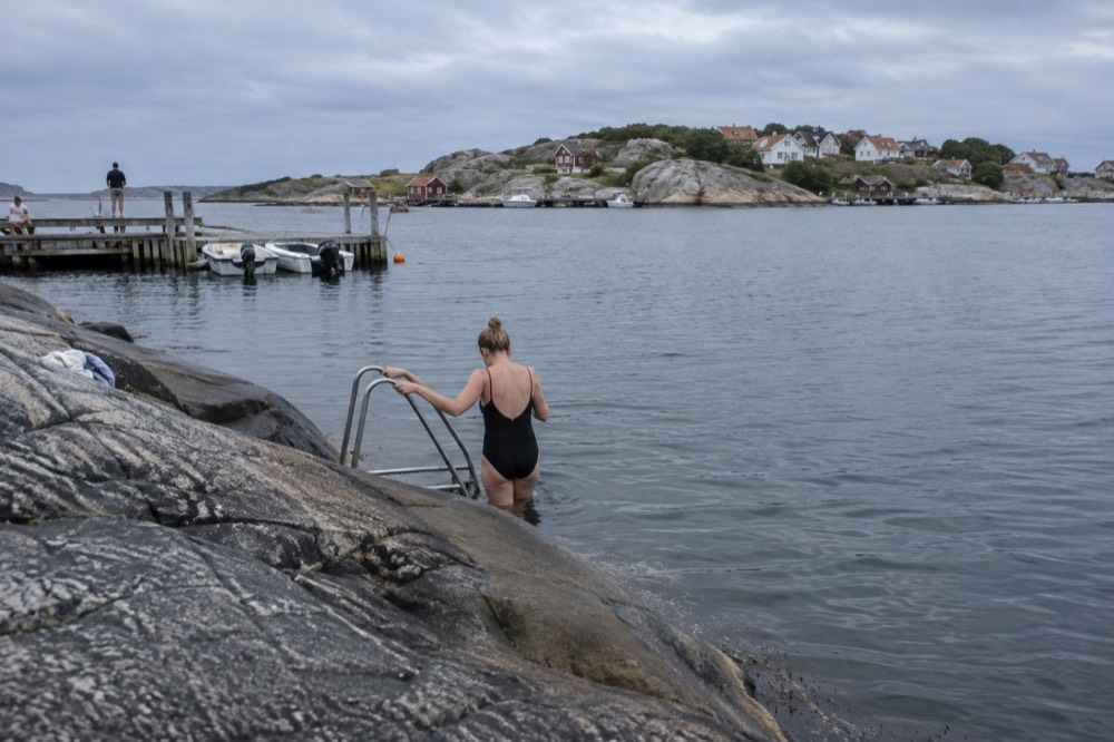 Swimmer entering calm blue sea from flat granite rocks in late summer