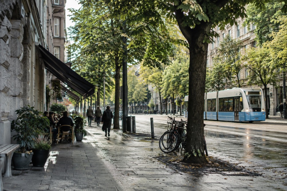 Stone apartment buildings lining a wide avenue in Vasastan, Gothenburg, with trees and a tram line visible