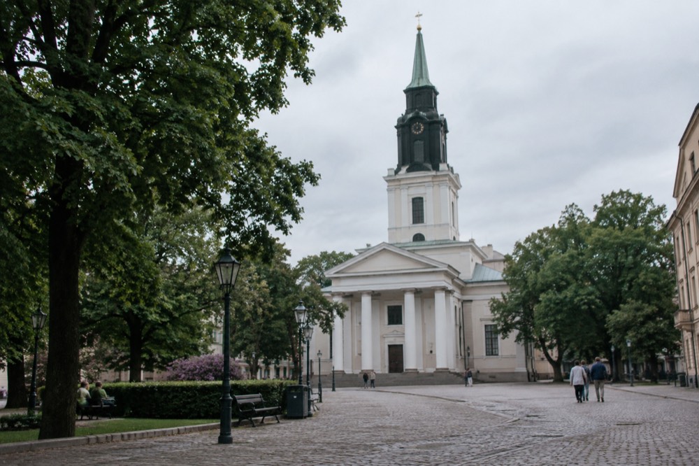 Gothenburg Cathedral's tall white classical facade seen from a cobbled square under a grey Nordic sky