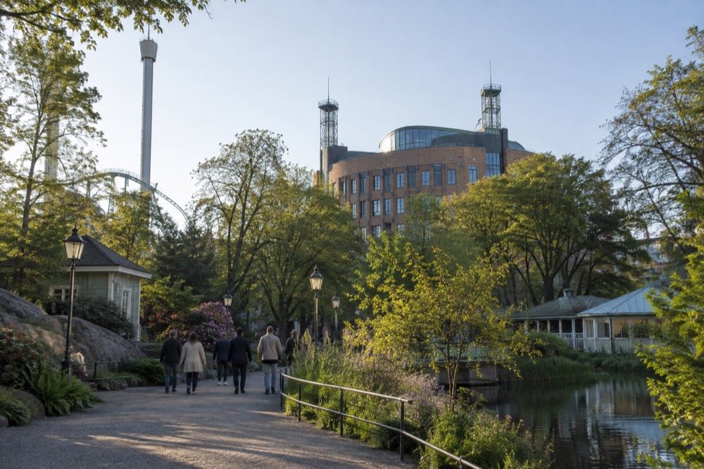 A hotel building with a curved brick facade and rooftop towers seen from a park path in daylight