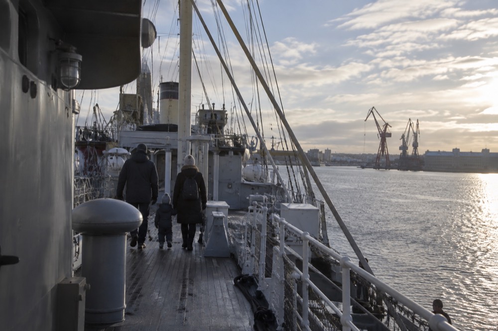 A family walking along the deck of a moored museum ship with railings and rigging