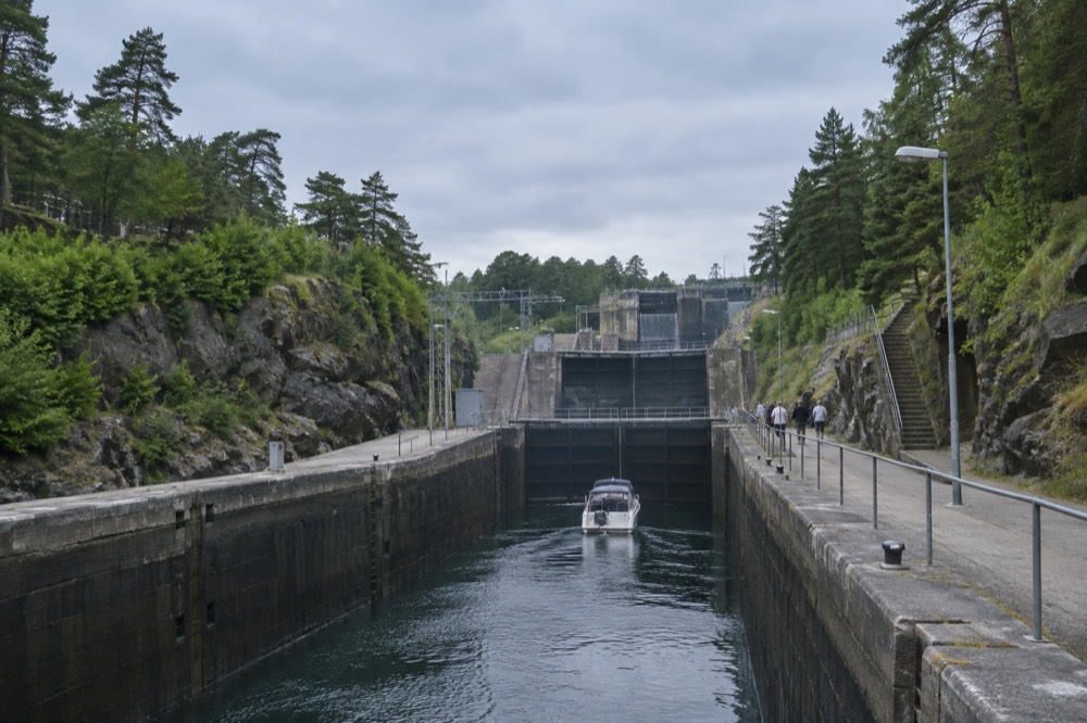A canal lock staircase in summer with green trees on both banks and a small boat in the chamber