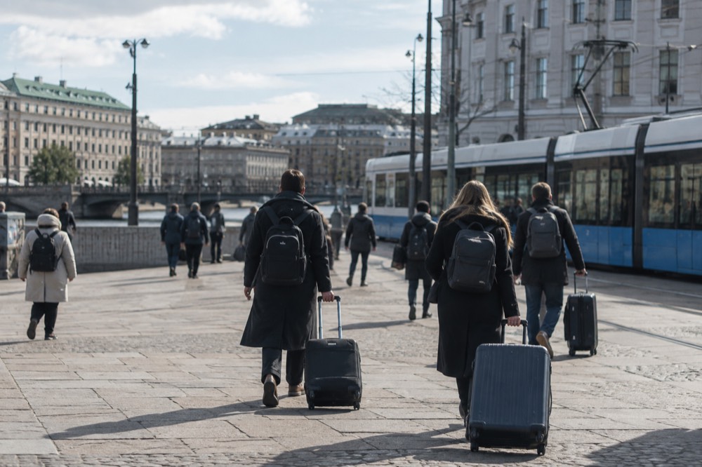 Passengers with luggage walking through a grand station hall toward tram stops outside