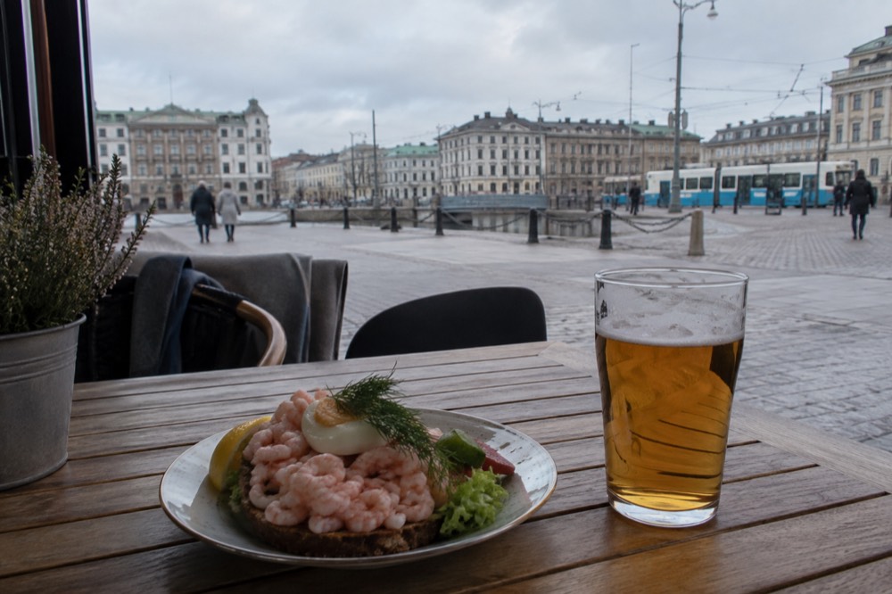 A shrimp sandwich and a glass of beer on a wooden table in a Gothenburg bar