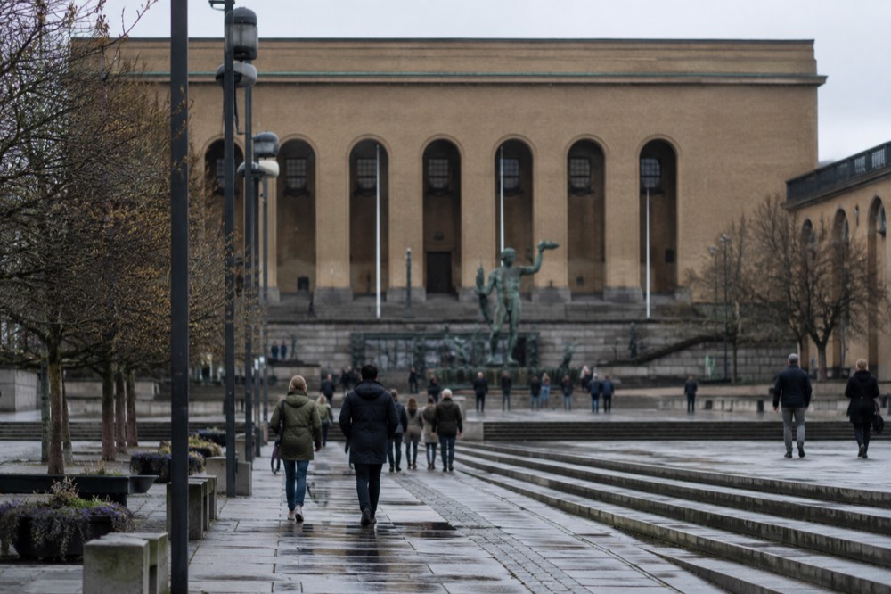 A stone art museum building on a wide avenue in Gothenburg with a statue in front and people walking past