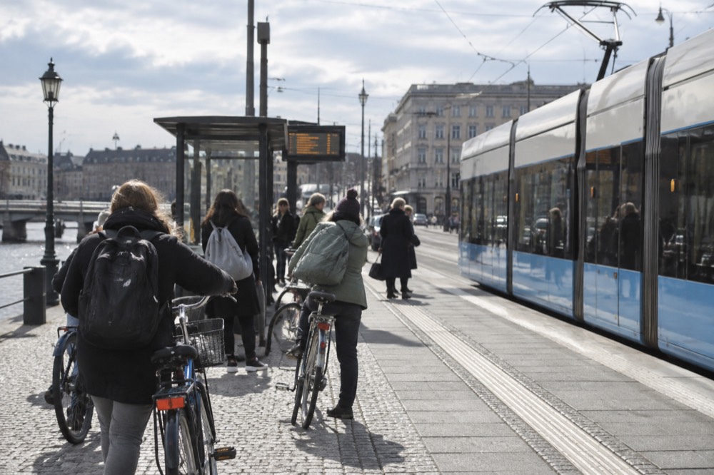 A tram stop in Gothenburg with a departure screen and cyclists waiting beside the platform