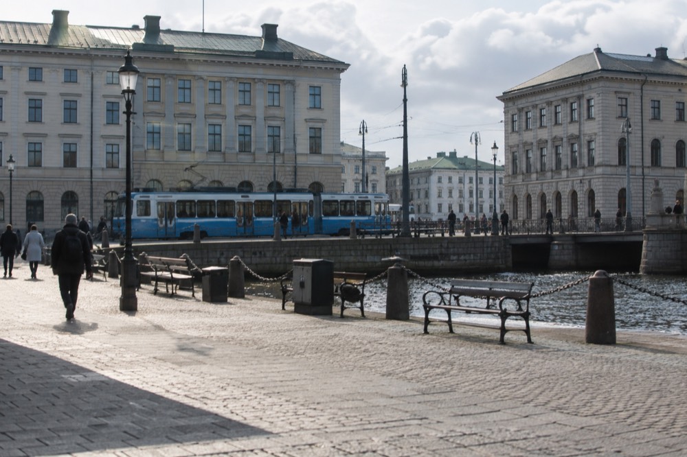 A vintage blue tram at a stop with granite buildings behind it