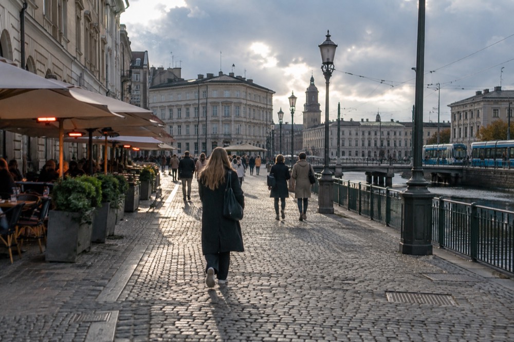 People walking a cobbled street between cafes in evening light