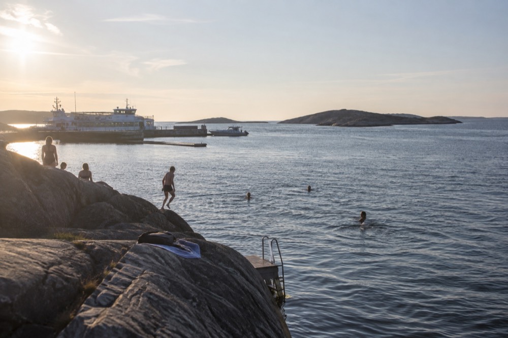 People swimming from a rocky ledge into calm blue sea at an island beach near Gothenburg