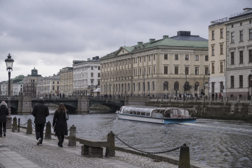 Gothenburg canal with a sightseeing boat passing stone buildings under a grey sky