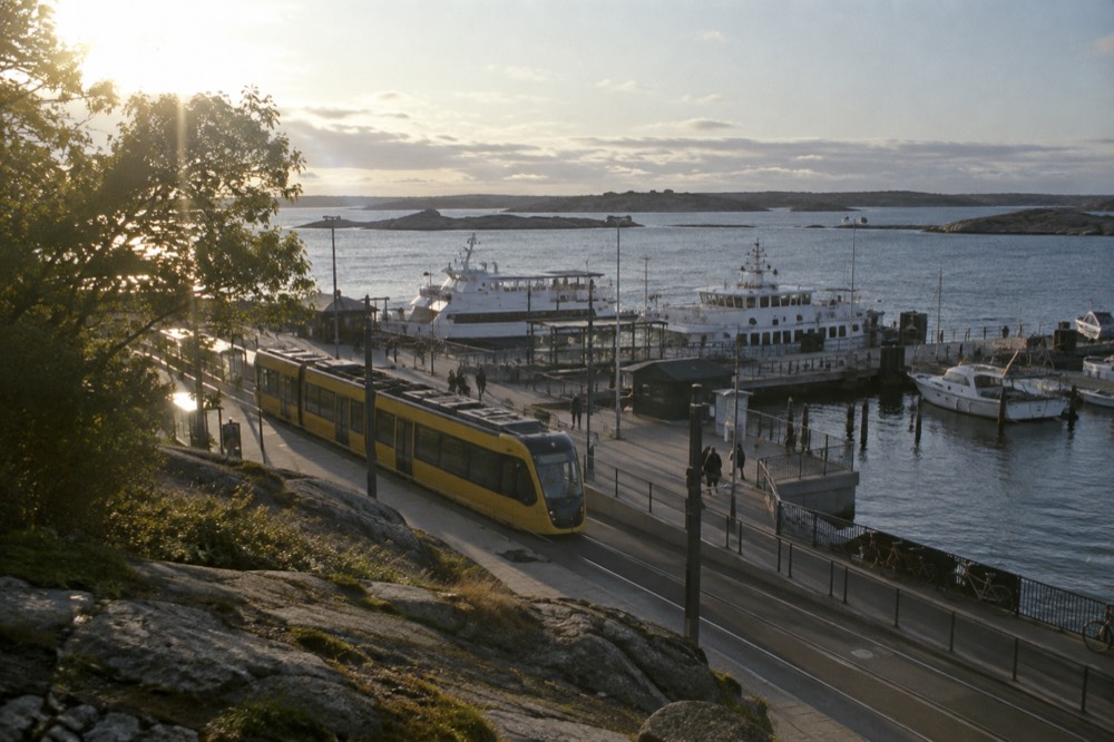 A yellow Gothenburg tram at a leafy waterfront terminus stop