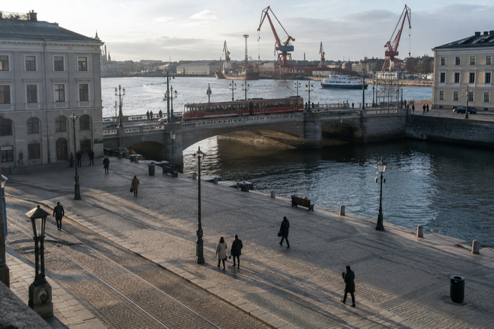 A red Gothenburg tram crossing a granite bridge near the harbour, with shipyard cranes behind it