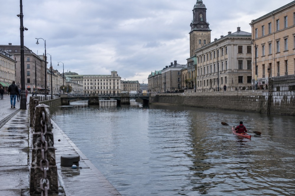 A kayak gliding along a canal in central Gothenburg with old stone warehouses on both banks