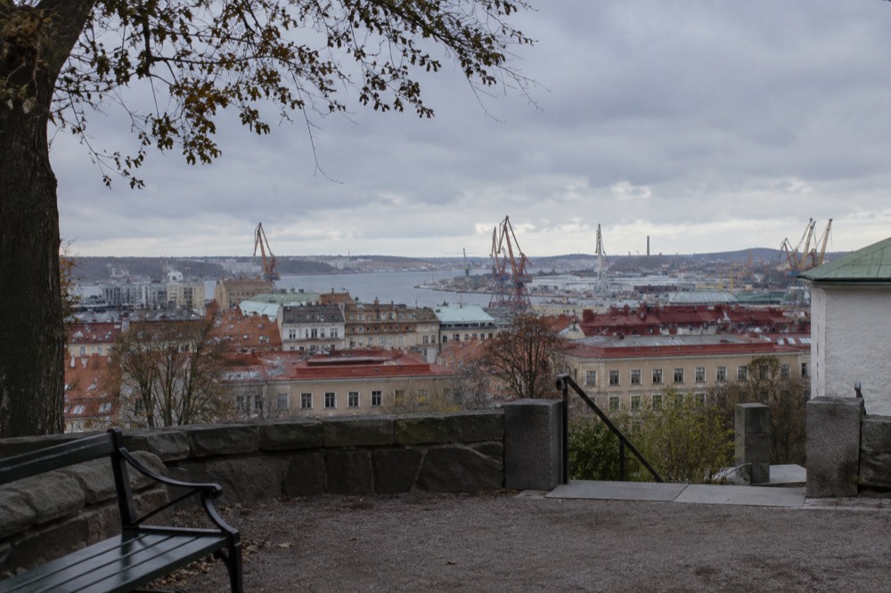 View over red rooftops and harbour cranes toward the sea from a hilltop churchyard