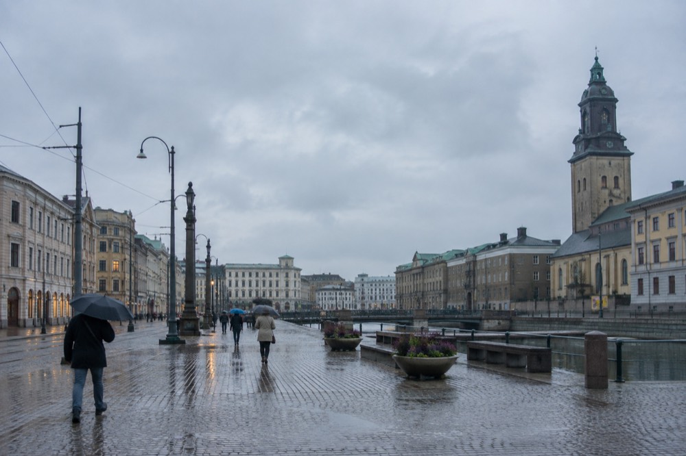Rainy Scandinavian street with wet cobblestones reflecting lights and people with umbrellas